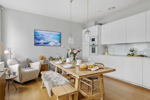 Una cocina moderna con armarios blancos, una mesa de comedor de madera y un televisor de pantalla plana grande montado en la pared.