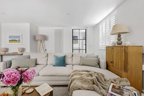 Una sala de estar moderna con sofá, lámpara, aparador de madera y ventana con persianas.