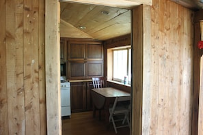 A wooden interior with a kitchen area, a dining table, and a window.