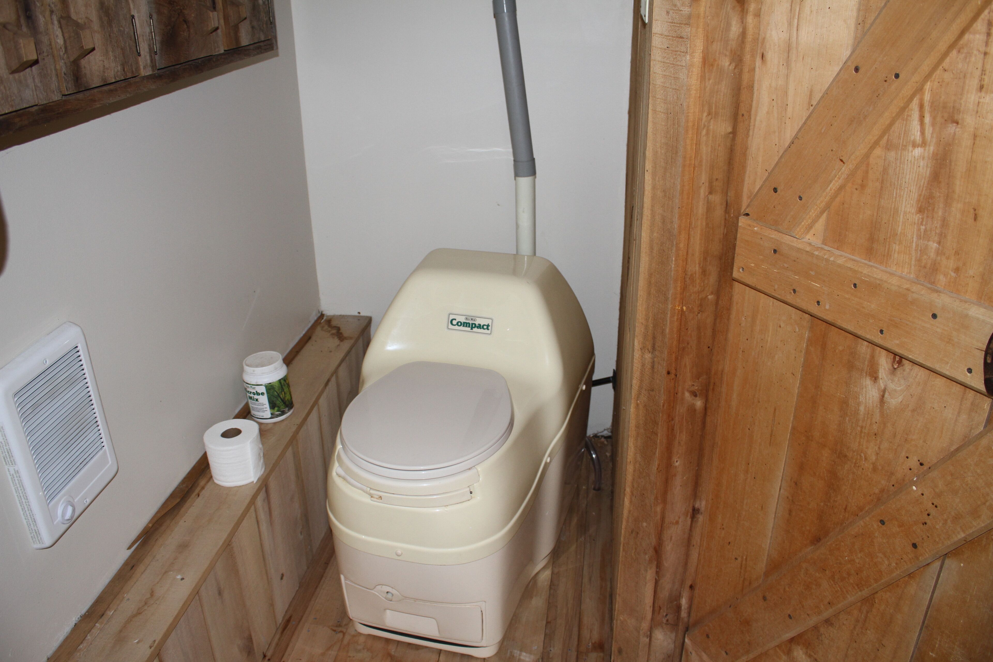 Des toilettes compactes avec un abattant blanc, un rouleau de papier toilette et un flacon de gel hydroalcoolique.