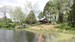 A lakeside cabin with a deck, surrounded by trees and a pond. - Peace Cabin- 20 min hike to Wilson Cave! (Deputy)