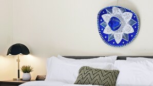 Cama bem arrumada com lençóis brancos, manta verde e cesta de fibra ao lado.