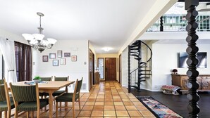 Uma sala de jantar com mesa e cadeiras de madeira, um candelabro e piso ladrilhado.