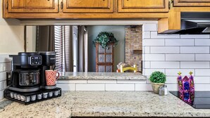 Cozinha com armários de madeira, cafeteira, caneca estampada, planta em vaso e objeto decorativo.