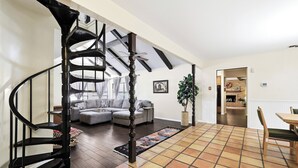Uma sala de estar com escada em espiral, área de jantar com mesa e cadeiras, e cozinha ao fundo.