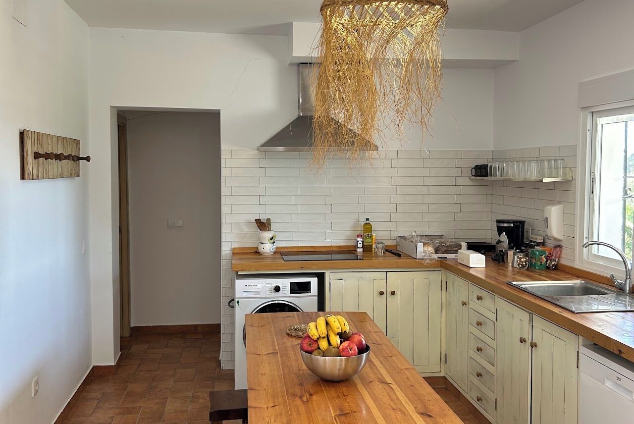 A modern kitchen with white tiles, a wooden countertop, a washing machine, and a fruit bowl.