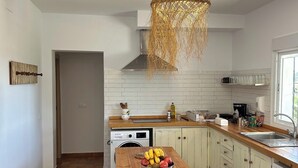 A modern kitchen with white tiles, a wooden countertop, a washing machine, and a fruit bowl.