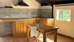 A kitchen with a brick backsplash, wooden cabinets, a wooden dining table, and a window with a view of greenery.