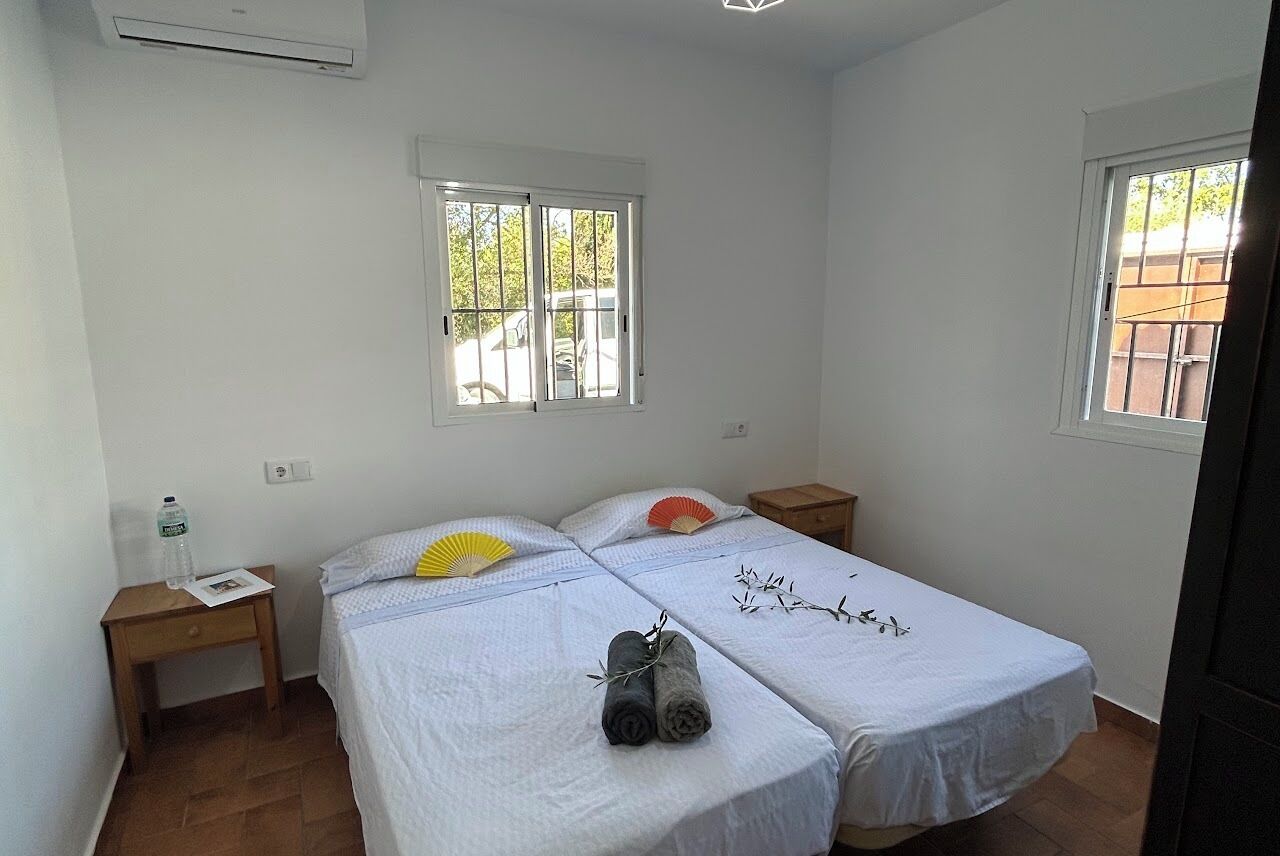 Una habitación con dos camas, una ventana, una mesita de noche de madera y un aire acondicionado instalado en la pared.