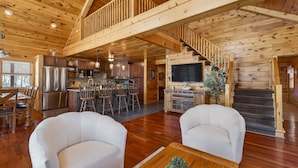 Un interior de cabaña de madera espacioso, con cocina, comedor y una escalera que lleva a un altillo.
