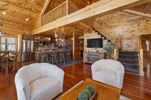 Ruim houten blokhutinterieur met keuken, eethoek en een trap naar een slaapzolder.