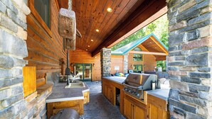 Una cocina al aire libre techada, con piso de piedra, armarios de madera y una parrilla.