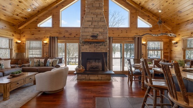Una cabaña de madera espaciosa con chimenea de piedra, muebles de madera y ventanas grandes.