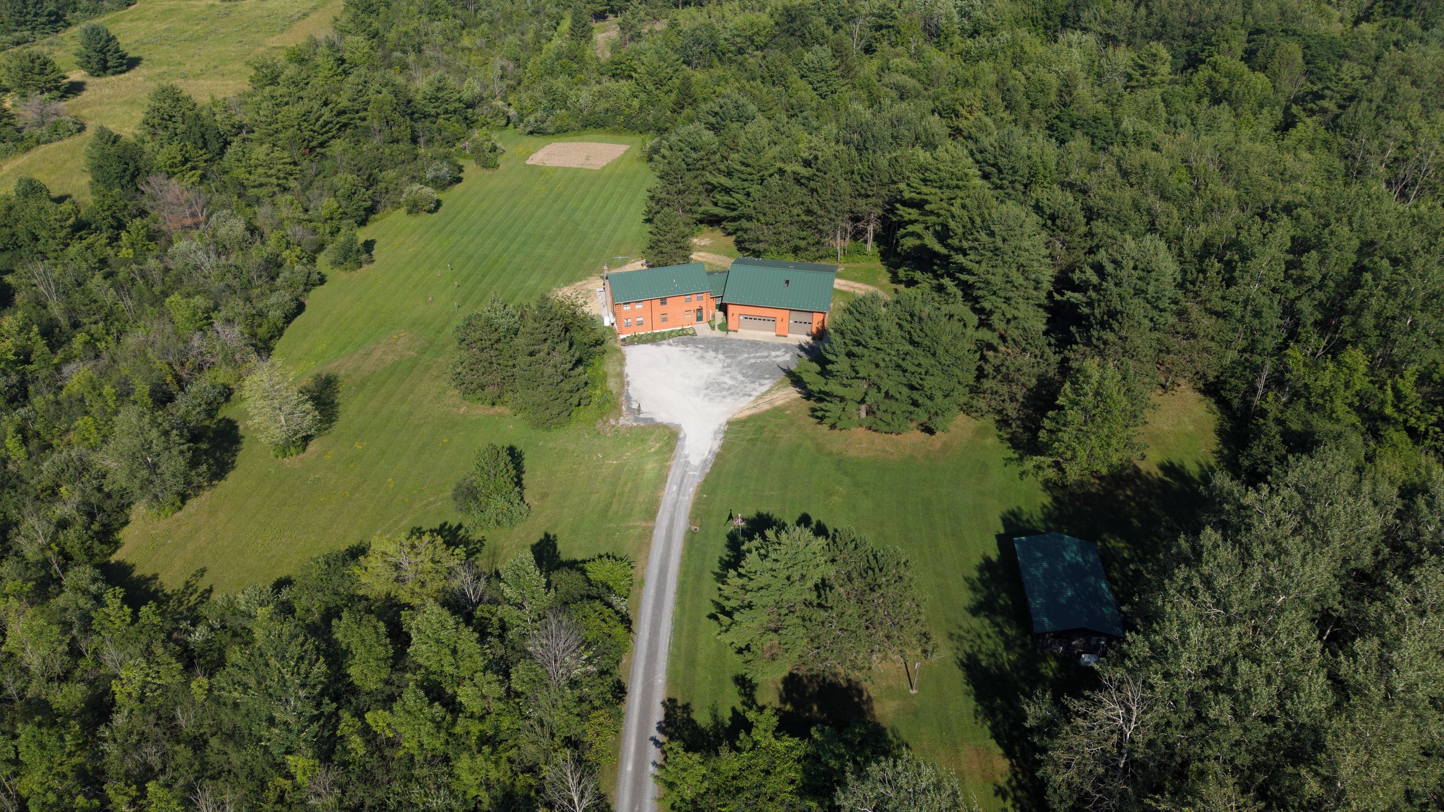An aerial view of a property with a large building, a driveway, and surrounding greenery.