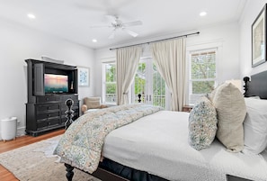 A bedroom with a bed, a television, a ceiling fan, and a window with curtains. - Fleur de Sea - Main House (Panama City Beach)