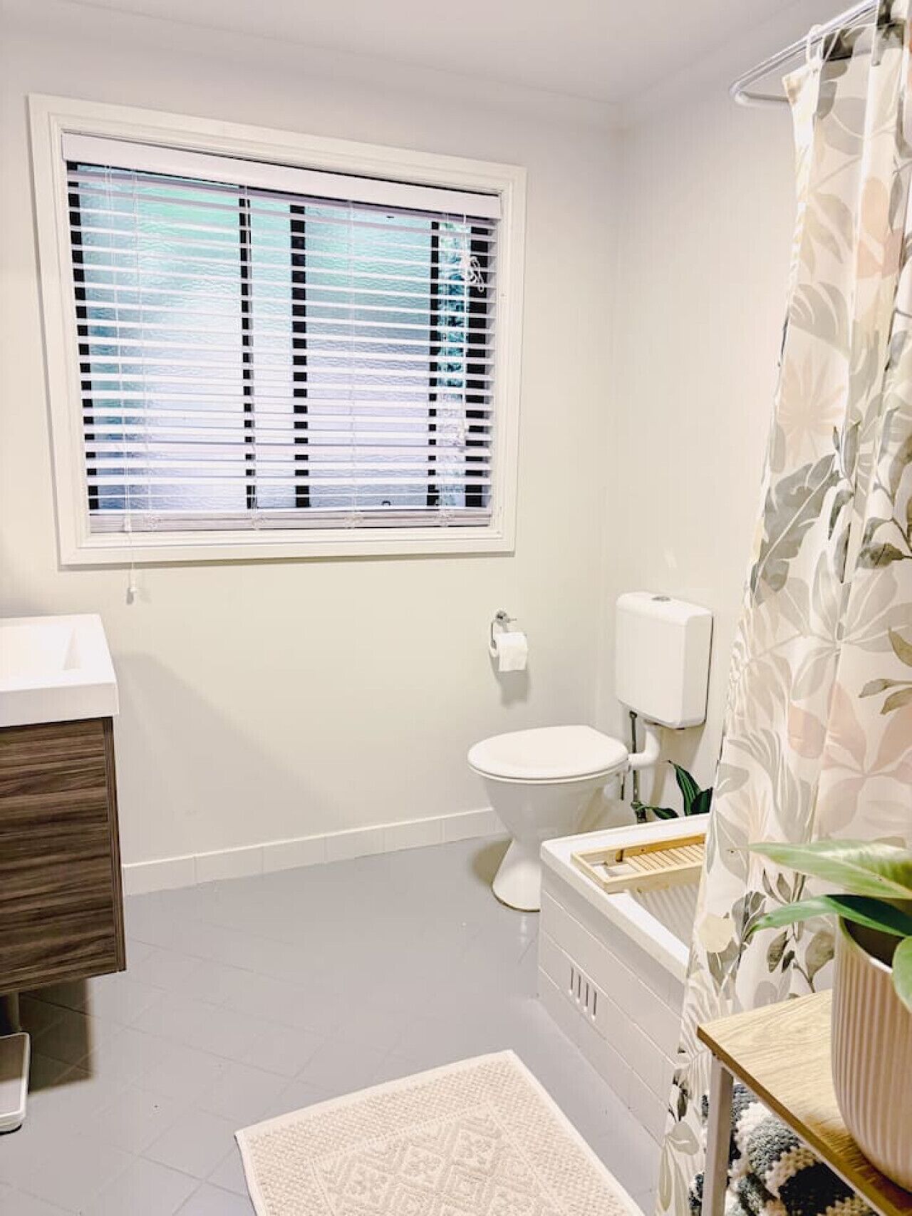 A bathroom with a toilet, a window with blinds, a shower curtain, and a sink.
