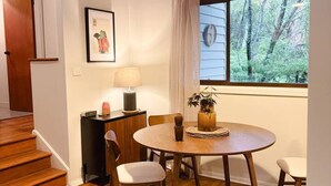 Uma área de refeições com mesa redonda, cadeiras, luminária pendente, janela com vista para árvores e uma escada.