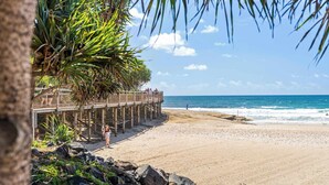 A beach with a wooden pier, rocky shoreline, and palm trees. - Happy Valley Tide - Bulcock Beachfront Apartment (Caloundra Region)