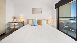 A hotel room with a bed, a desk, a chair, a ceiling fan, a painting, and a view of the outside. - Happy Valley Tide - Bulcock Beachfront Apartment (Caloundra Region)