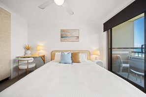 Une chambre d’hôtel avec un lit, un bureau, une chaise, un ventilateur de plafond, un tableau et une vue sur l’extérieur.