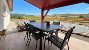 Eine Terrasse im Freien mit Tisch und Stühlen, ein rotes Dach und Blick ins Grüne.