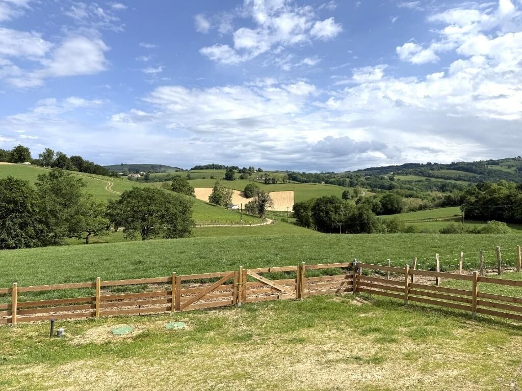 A rural landscape with rolling hills, a wooden fence, and a clear sky.