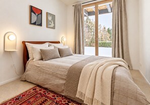 A bedroom with a bed, two wall-mounted lights, a window with curtains, and a rug. - Historic Mazot Retreat by Mrs Miggins – Charming Alpine Stay in Crans-MontanaHistoric Mazot Retreat (Lens)