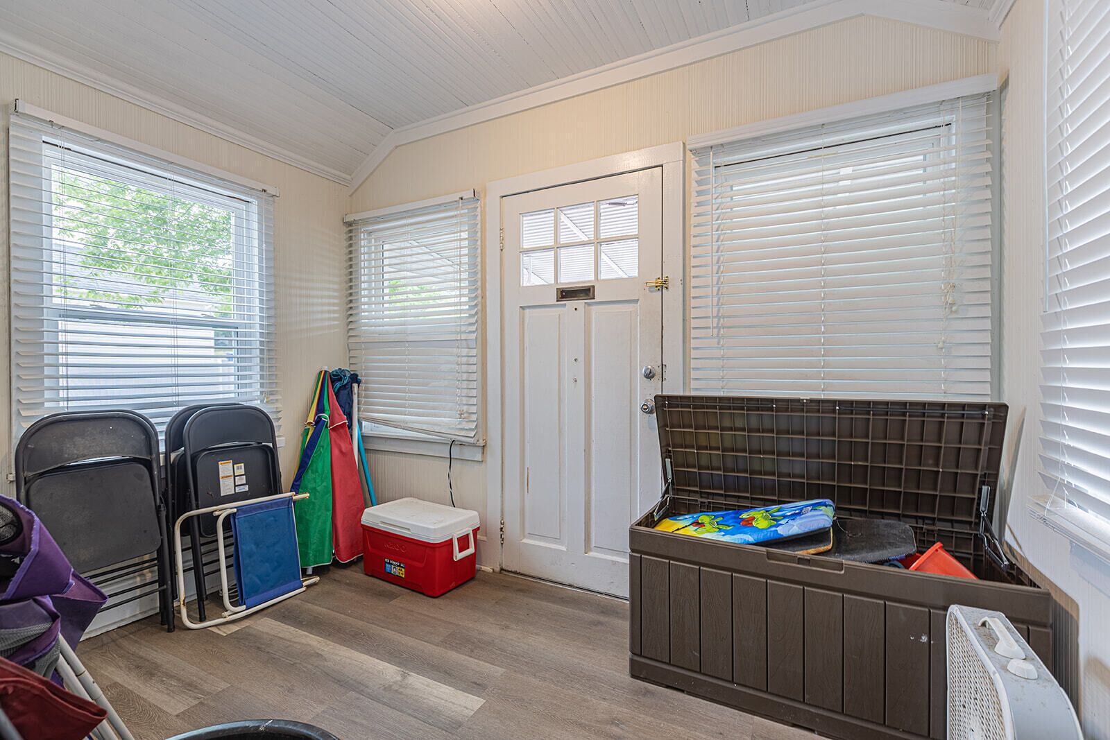A compact room with a bed, a small table, a fan, and a window with blinds.