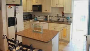 A kitchen with white cabinets, a granite countertop island, a refrigerator, and a microwave. - Renovated 3BR Shore House • Yard, Porch & Bay Breezes • Pet Friendly (Ocean City)