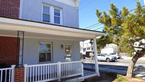 A two-story building with a white porch and a brick facade. - Renovated 3BR Shore House • Yard, Porch & Bay Breezes • Pet Friendly (Ocean City)