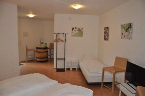 A room with two beds, a chair, a small table, a coat rack, and a television. - Comfort Hotel Egerkingen (Egerkingen)