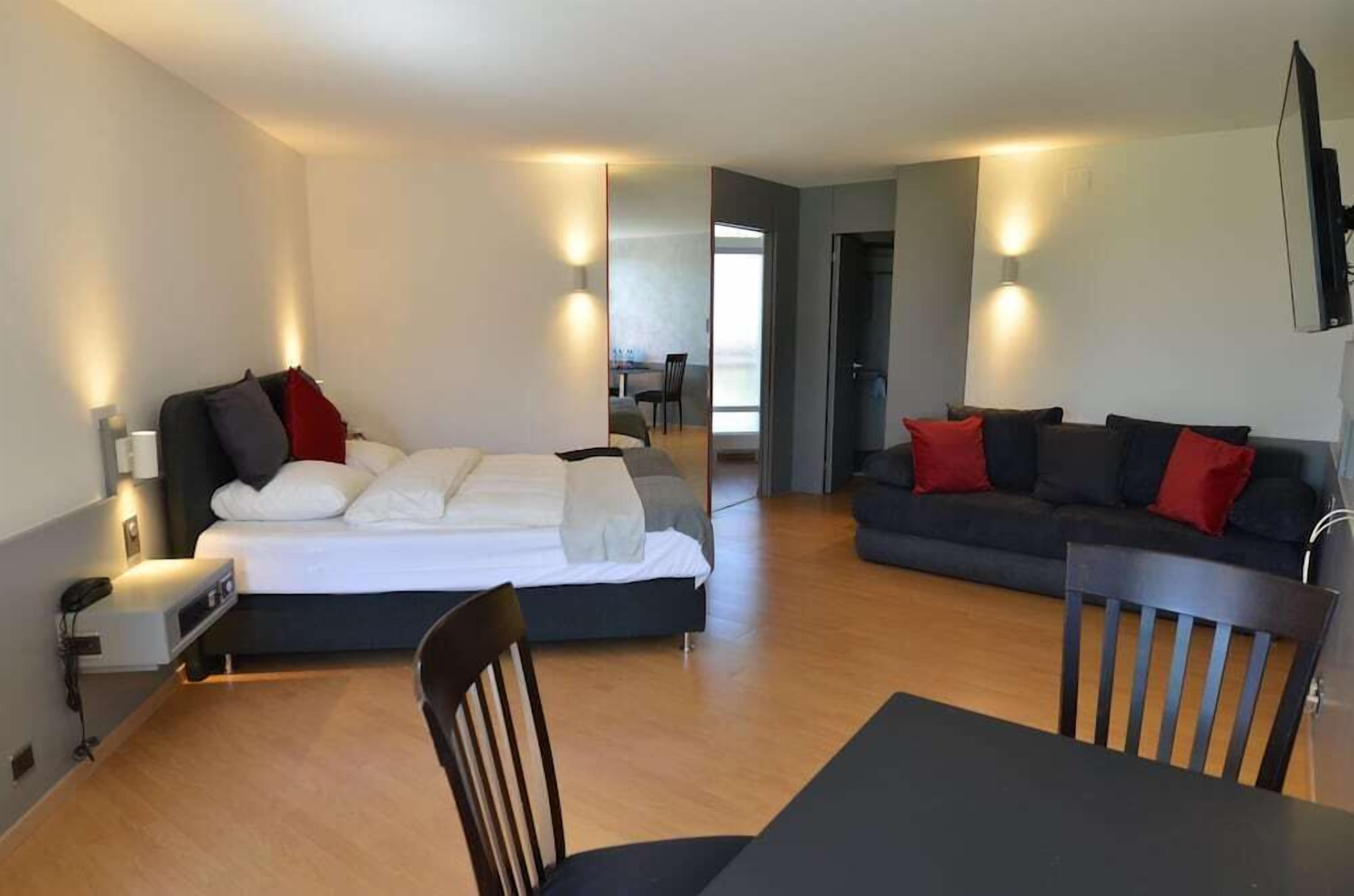 Ett modernt hotellrum med en säng, en soffa, ett matbord och en tv.