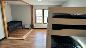 A room with a bunk bed, a small desk, a window with blinds, and a wooden floor.