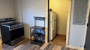 A compact kitchen with a stove, a small shelf, and a refrigerator.