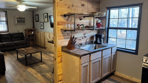 A cozy living room with a wooden ceiling and a kitchen area featuring a built-in island with a sink and coffee maker.