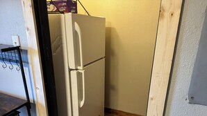 A compact kitchen with a white refrigerator, wooden flooring, and a small countertop with a power strip.