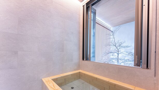A modern bathroom with a glass-enclosed shower, light-colored tiles, and a window with blinds. - Hakone Seiun (Hakone)