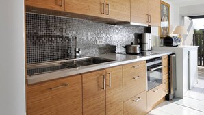 Eine moderne Küche mit Holzausstattung, einer gefliesten Spritzschutzleiste, Edelstahlgeräten und einem eingebauten Backofen.