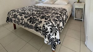 Ein Schlafzimmer mit Bett, Holzschrank, Nachttisch, Lampe und einem gerahmten Bild an der Wand.