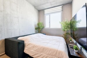 A modern bedroom with a bed, a dark bench, a window, and two potted plants.