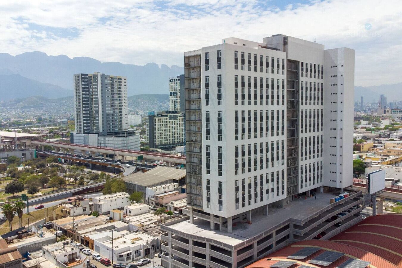 A modern high-rise building with multiple floors, surrounded by other buildings and a highway.