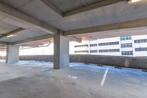An empty parking garage with concrete pillars, marked parking spaces, and a view of a white building with multiple windows.