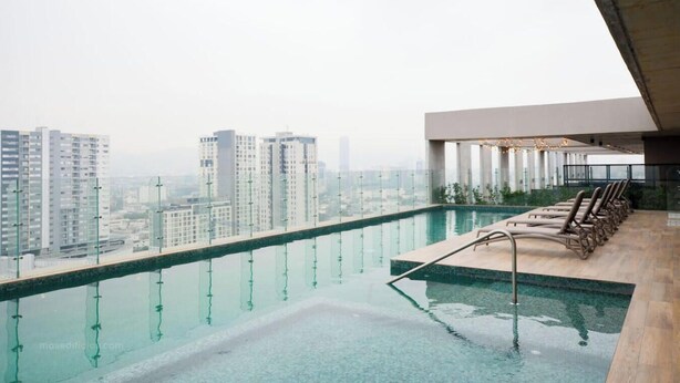 Una piscina infinita en la azotea con vistas a rascacielos, sillas de descanso y un diseño arquitectónico moderno.