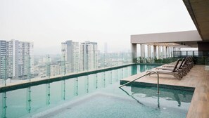 A rooftop infinity pool with a view of high-rise buildings, lounge chairs, and a modern architectural design.