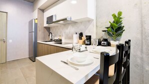 Una cocina moderna con muebles blancos, horno empotrado, cafetera y comedor con mesa dispuesta para dos.