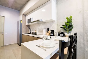 A modern kitchen with white cabinetry, a built-in oven, a coffee machine, and a dining area with a table set for two.