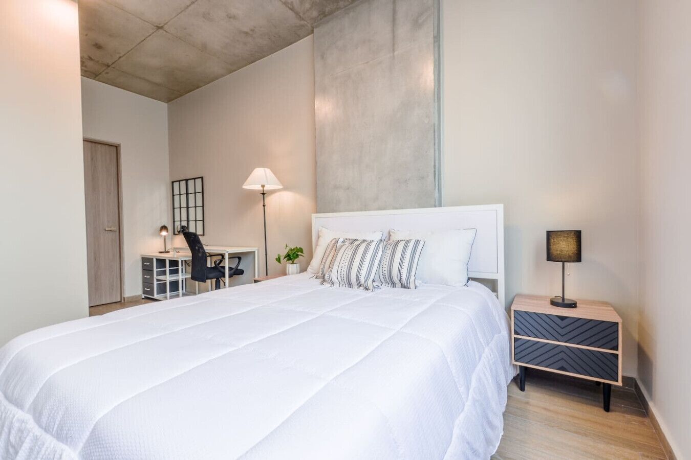 A bedroom with a large bed, a desk, a chair, a lamp, and a nightstand.