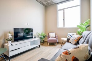 Ein Wohnzimmer mit Flachbildfernseher, einer Couch, einem Sessel und Topfpflanzen.