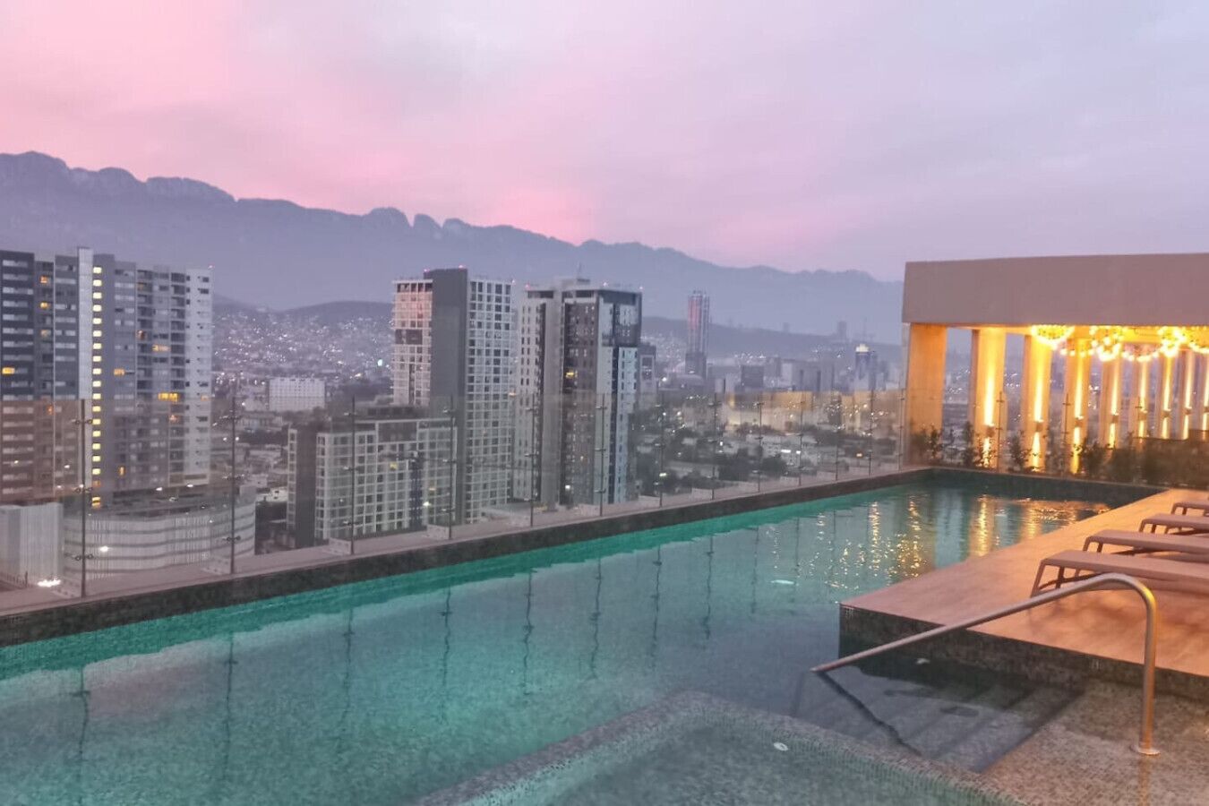 A rooftop pool with a cityscape view, including high-rise buildings and mountains in the background.