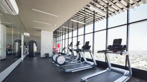 Un gimnasio con cintas de correr, bicicletas estáticas y una máquina de remo, con amplias ventanas que ofrecen vistas de la ciudad.